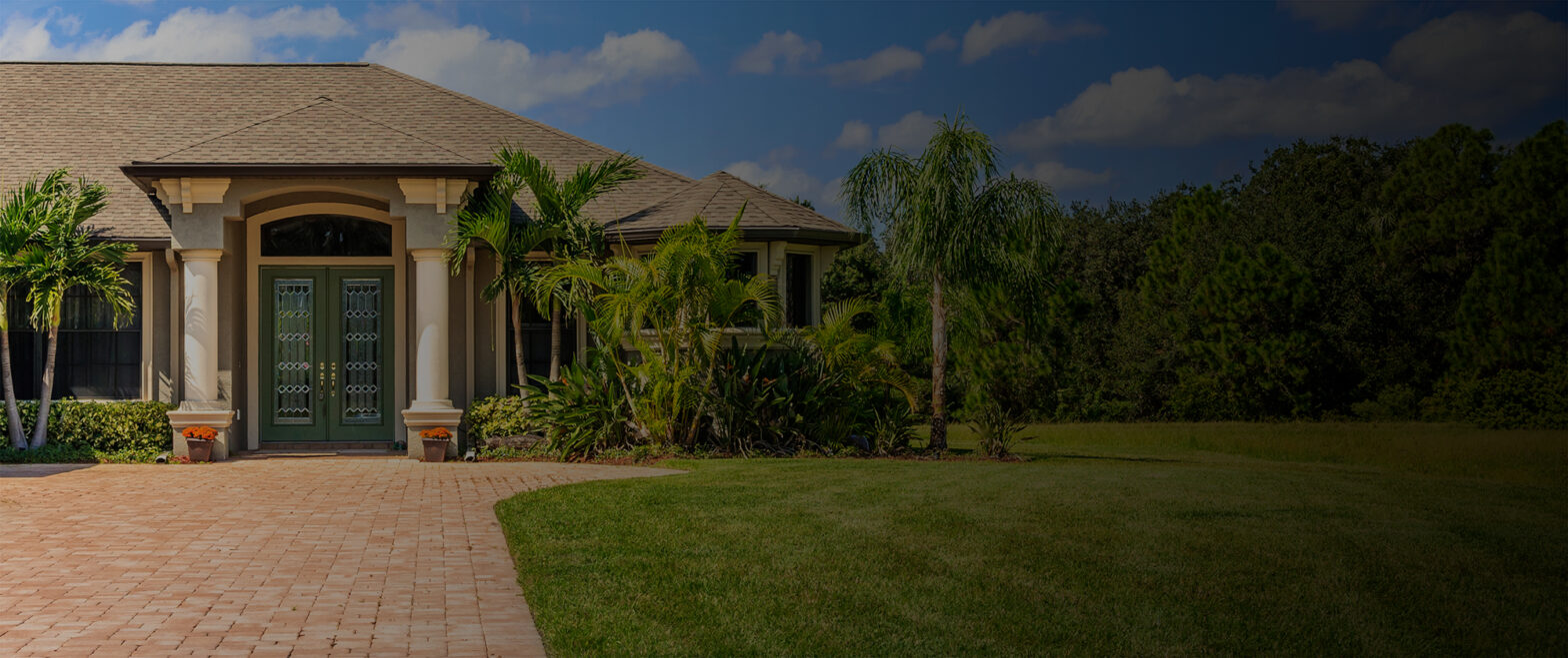 A sunny suburban house with a well-kept lawn and palm trees.